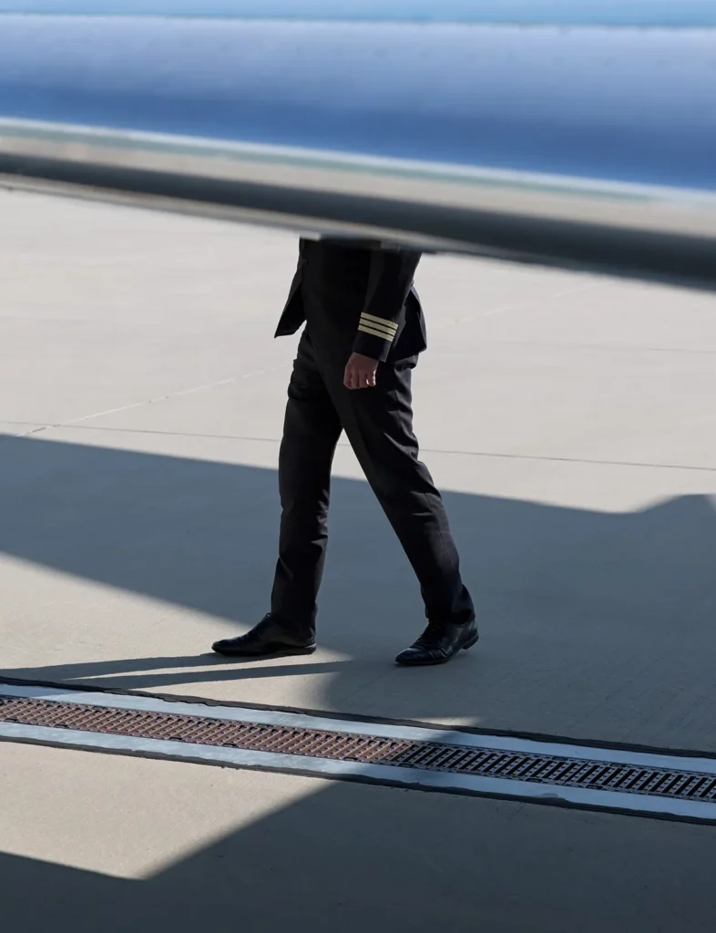 A pilot in uniform, partially obscured by an aircraft wing, walking on the tarmac during a routine inspection, highlighting the role of thorough checks.