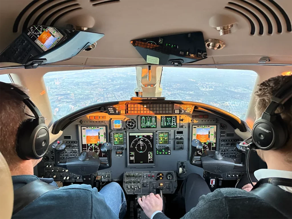 Two pilots in the cockpit of an aircraft, surrounded by advanced flight instruments and controls, demonstrating how technology aids in streamlining aviation.