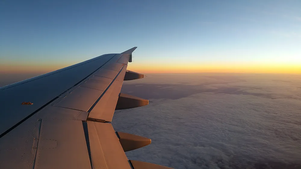 A view from the airplane window showing the wing, clouds, and a beautiful sunrise over the horizon, symbolizing the smooth and efficient journeys enabled by streamlining aviation.